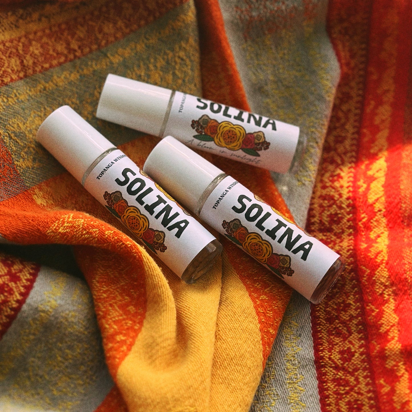 Three lip balm tubes with 'SOLINA' branding on a colorful fabric background