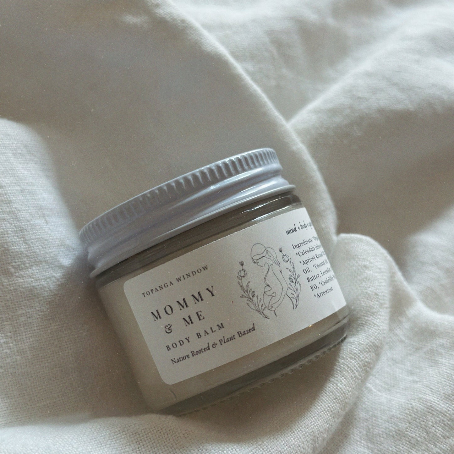 Jar of 'Mommy & Me' body balm on a white fabric background