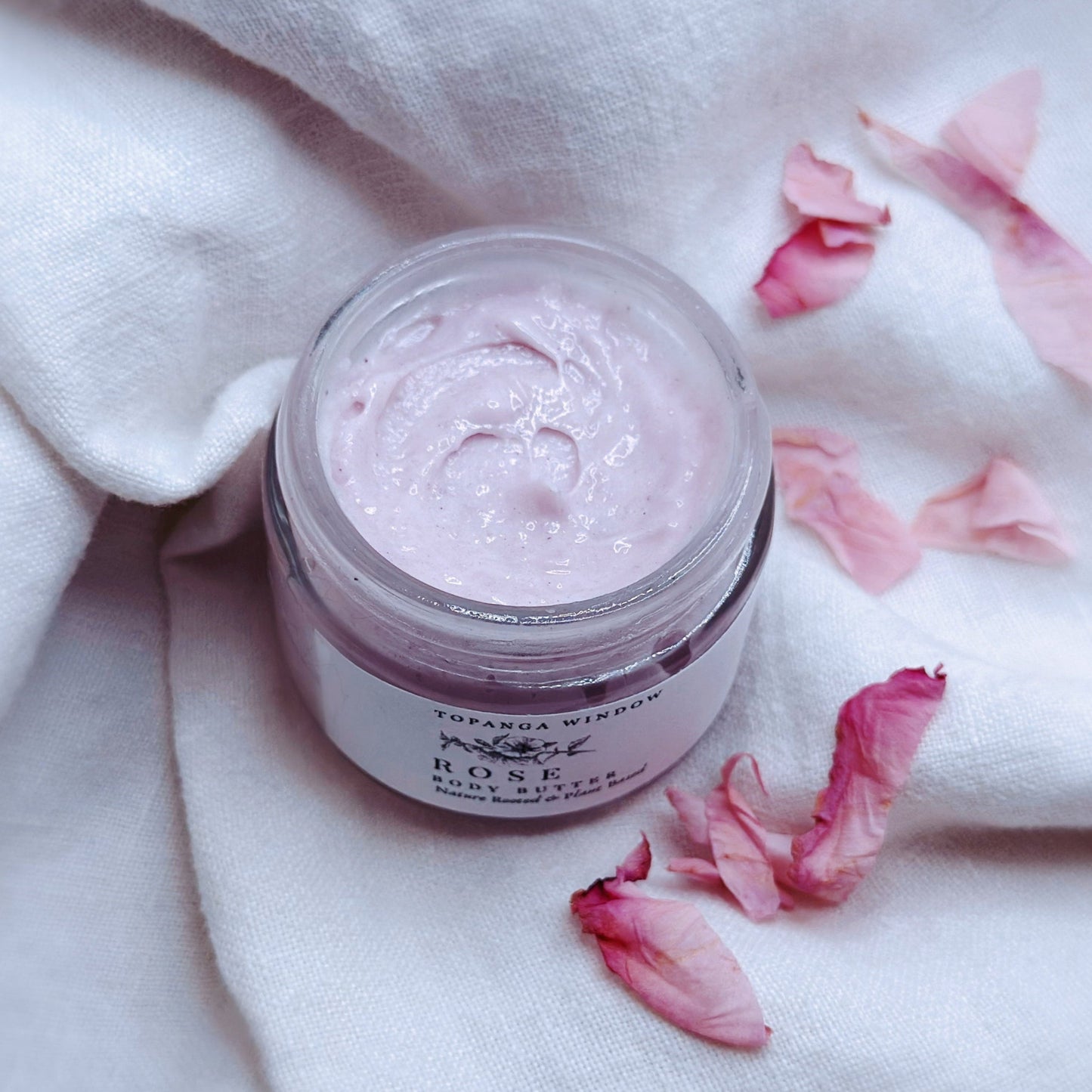 Pink skincare product jar on a white fabric background with pink petals