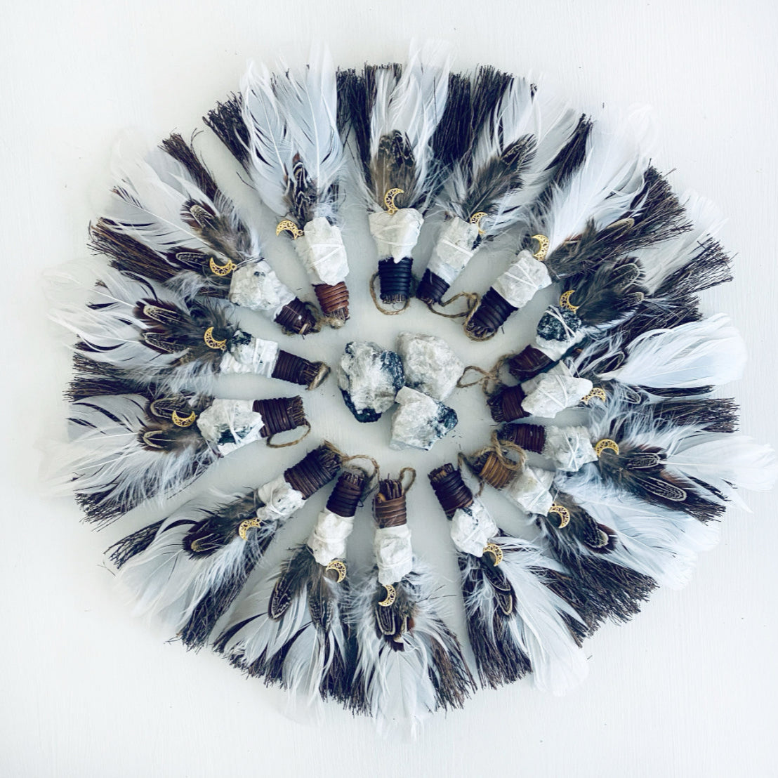 Decorative mini besom brooms with feathers and stones on a white background