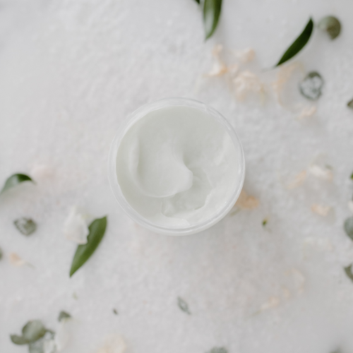 jar of body balm with a white cap on a light background with green leaves