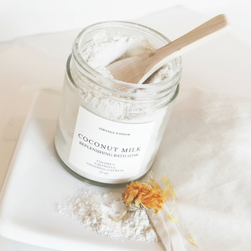 Jar of coconut milk bath salt with a wooden spoon on a white surface