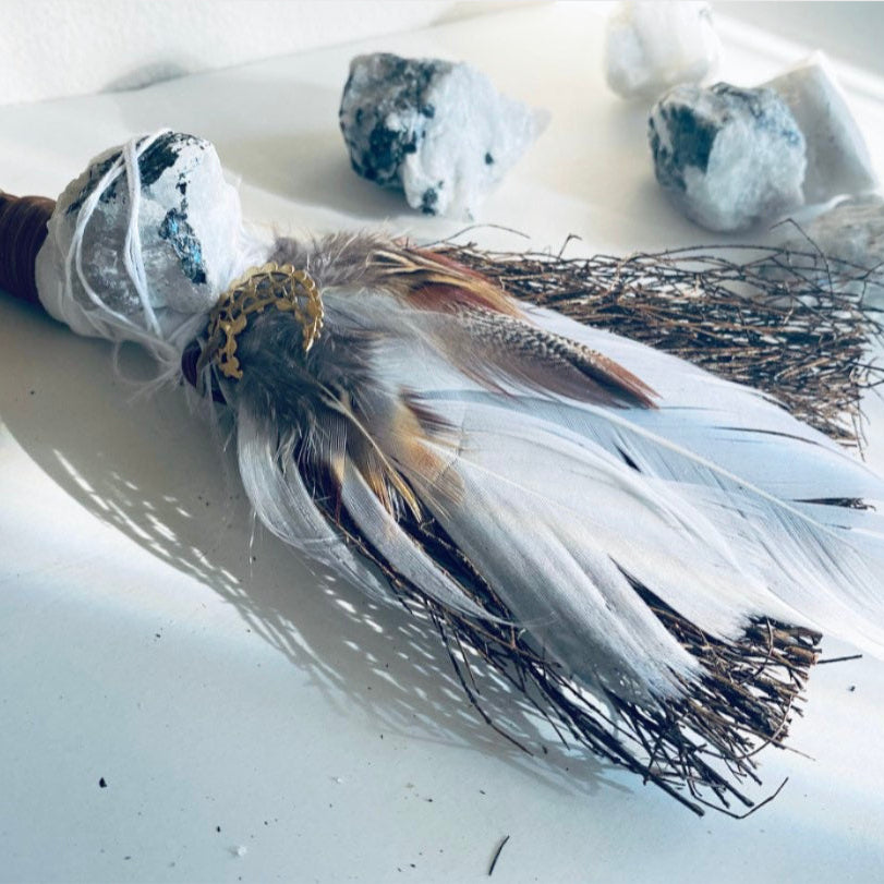 Decorative broom with feathers and stones on a light background