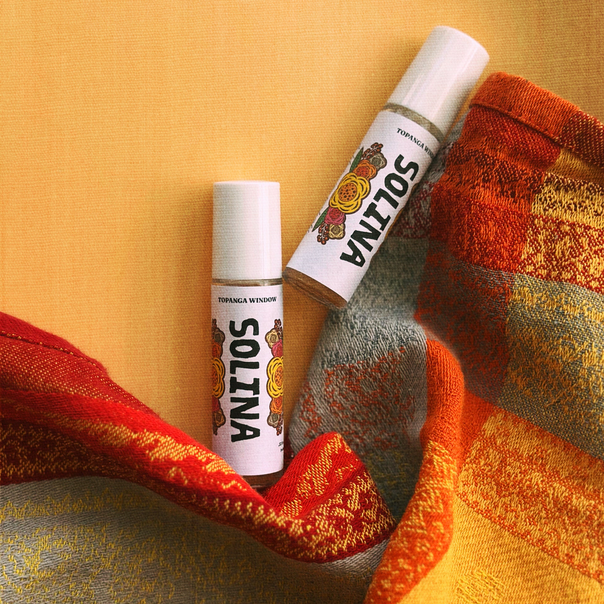Two Solina lip balm tubes on a textured fabric background