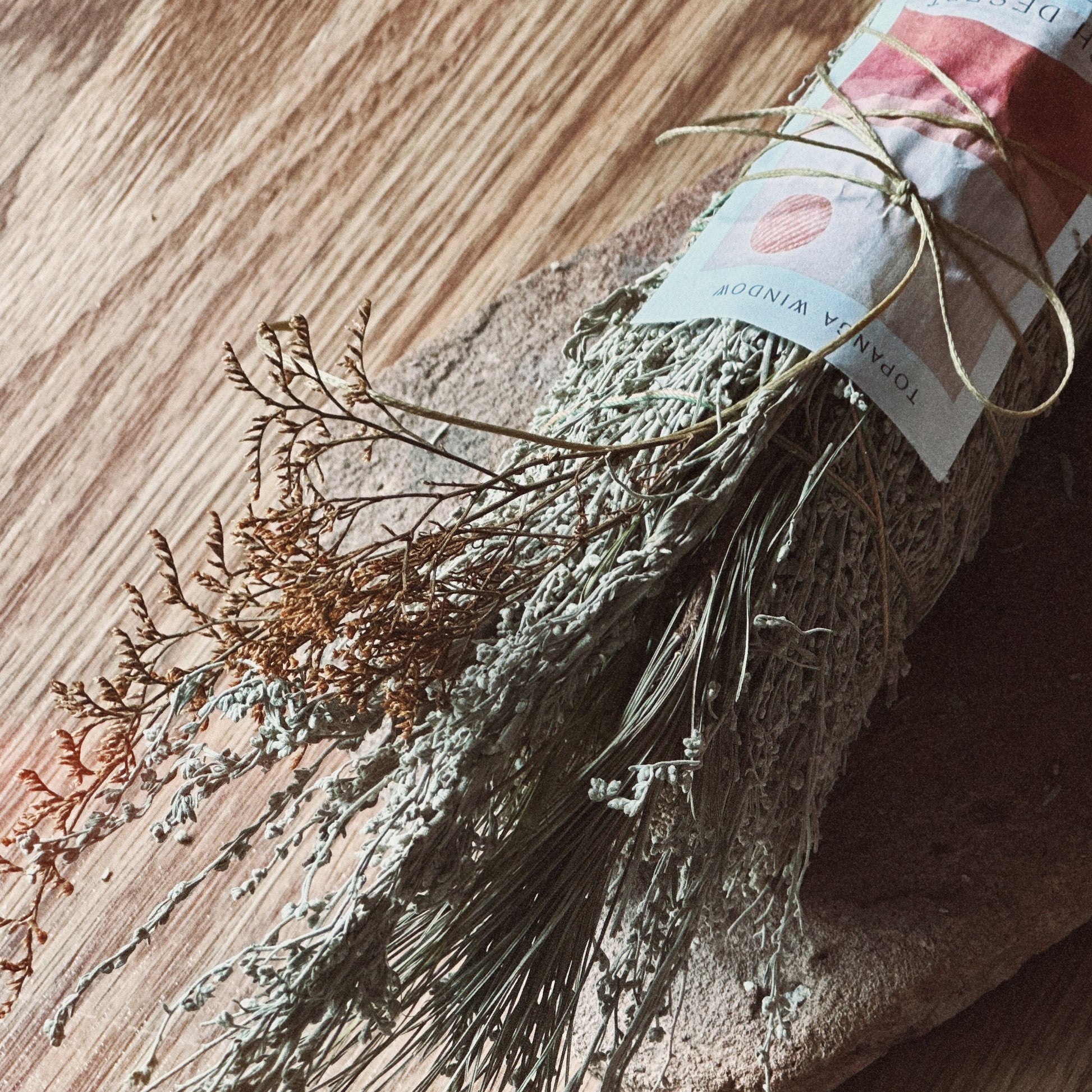 A bundle of dried botanical herbs wrapped in burlap and tied with twine, featuring a paper label, resting on a rustic stone slab over a wooden surface.