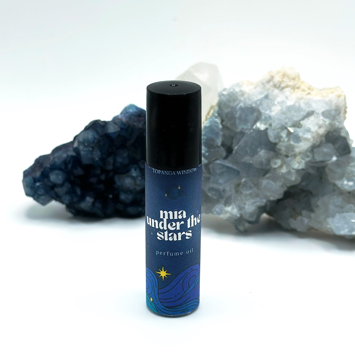 Perfume oil bottle labeled 'mia under the stars' with decorative rocks in the background