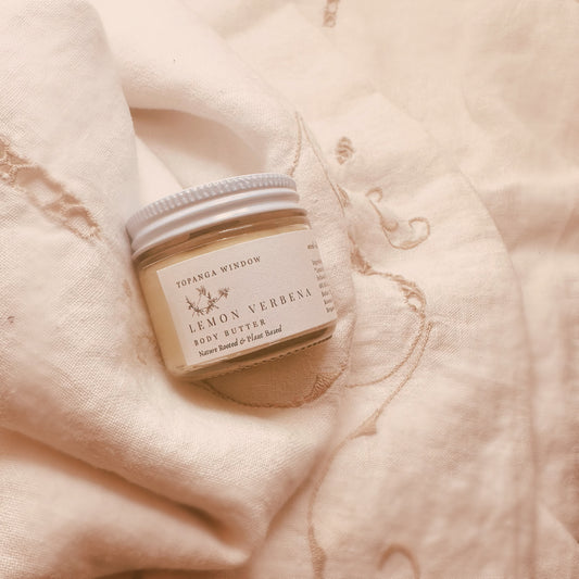 Jar of lemon verbena body butter on a soft fabric background