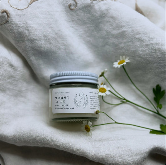 Small jar of 'Mommy & Me' balm on a textured fabric surface with flowers.