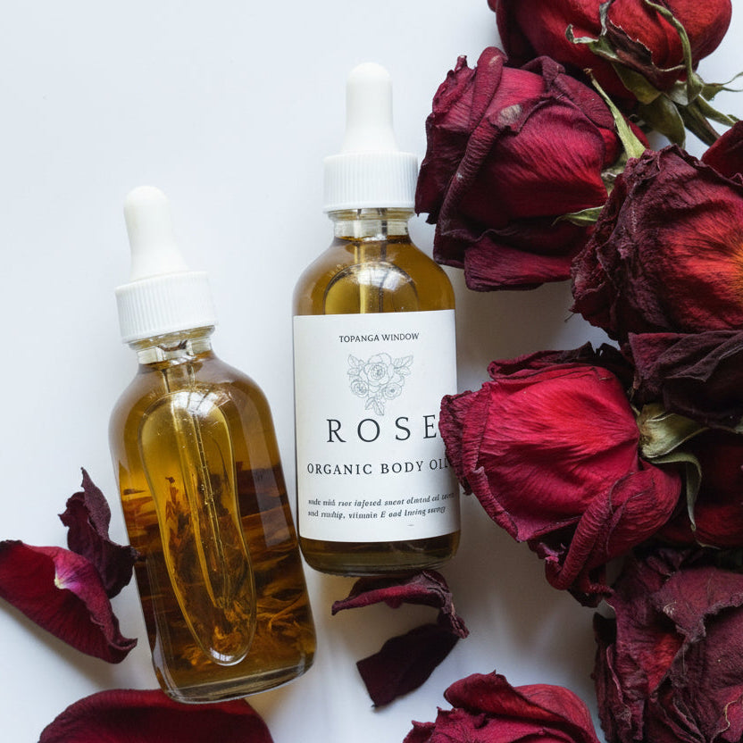 Two bottles of organic body oil with dried roses on a white background