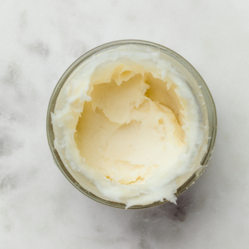 Glass jar filled with a white cream or butter on a marble surface