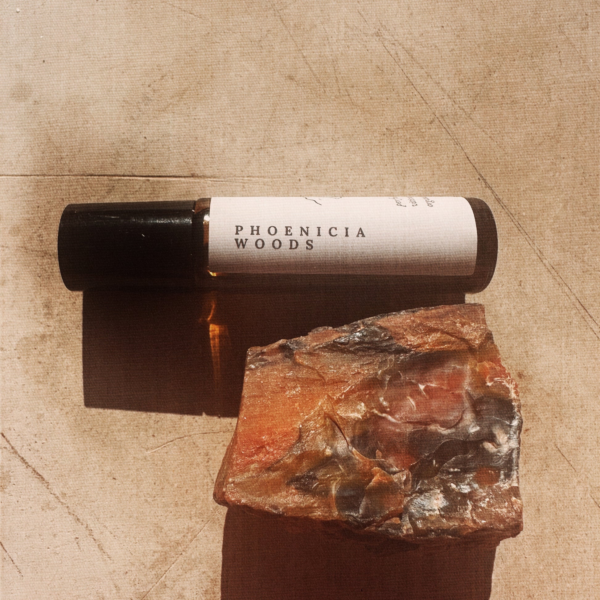 Roll-on bottle labeled 'Phoenicia Woods' on a textured surface with a stone.