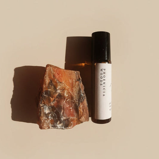 Roll-on bottle labeled 'Phoenicia Woods' on a textured surface with a stone.