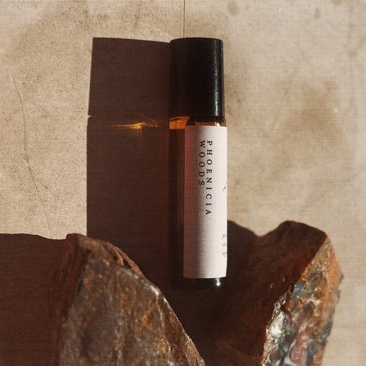 Roll-on bottle labeled 'Phoenicia Woods' on a textured surface with rocks.