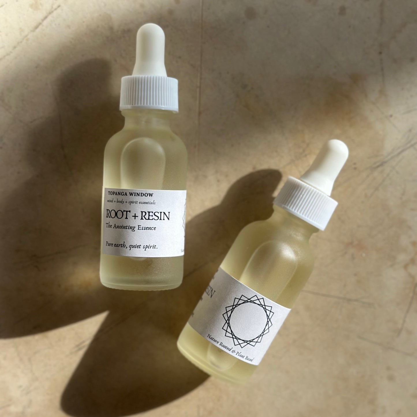 Two dropper bottles labeled 'Root + Resin' on a textured surface.