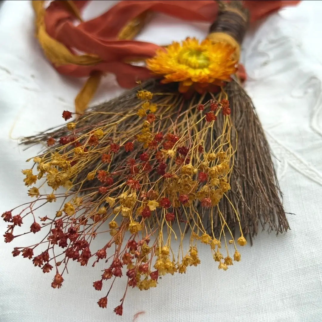 Decorative broom with dried flowers and ribbons on a white background