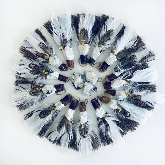 Decorative mini besom brooms with feathers and stones on a white background