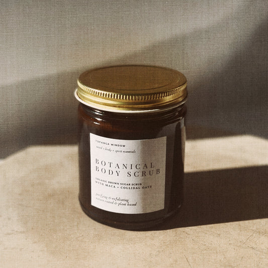 Jar of botanical body scrub with a gold lid on a textured surface