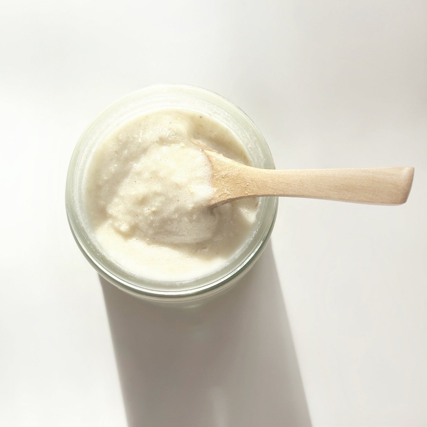 Jar of coconut milk body scrub with a wooden spoon on a white background
