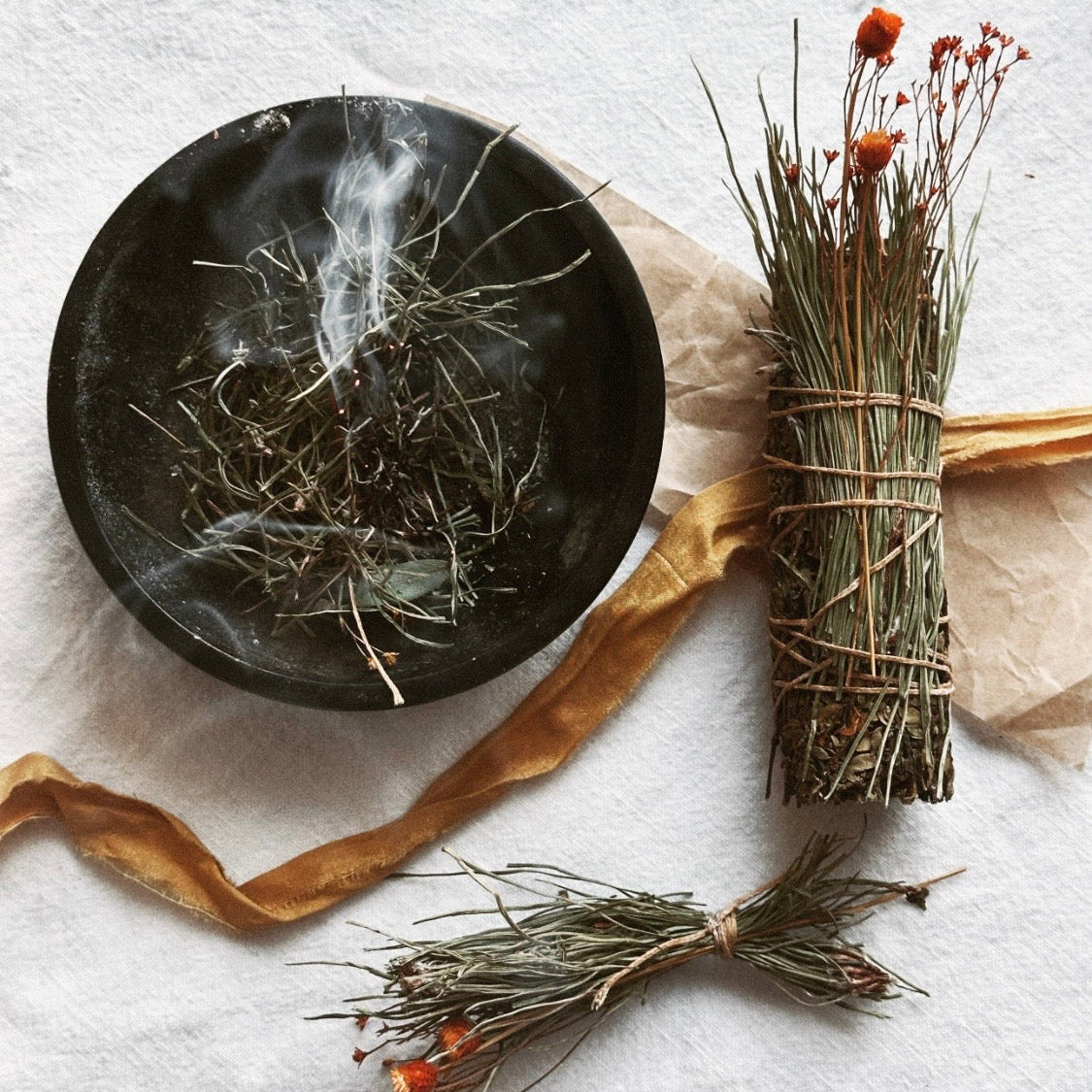 Dried herbs and a black plate on a textured white surface
