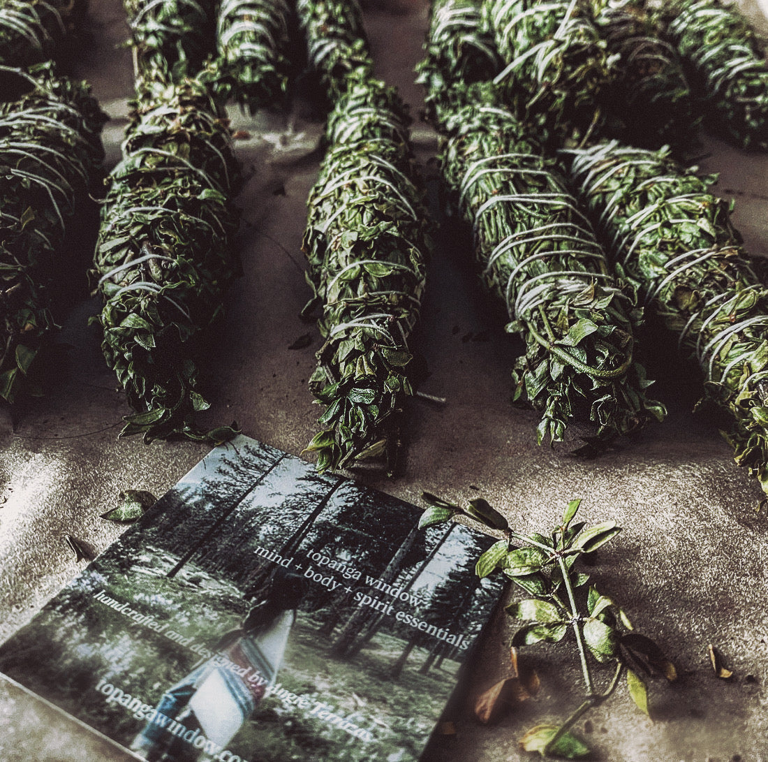 Bundles of sage on a textured surface with a magazine titled 'topanga indigo' partially open.