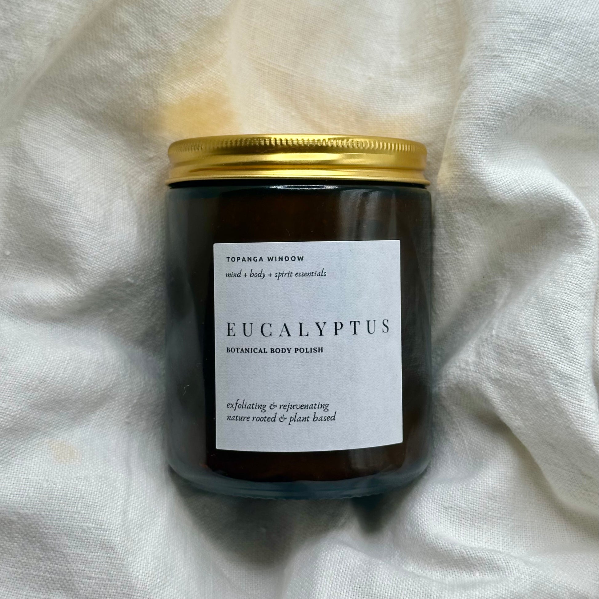 sugar scrub jar  with a gold lid and 'Eucalyptus' label on a white fabric background