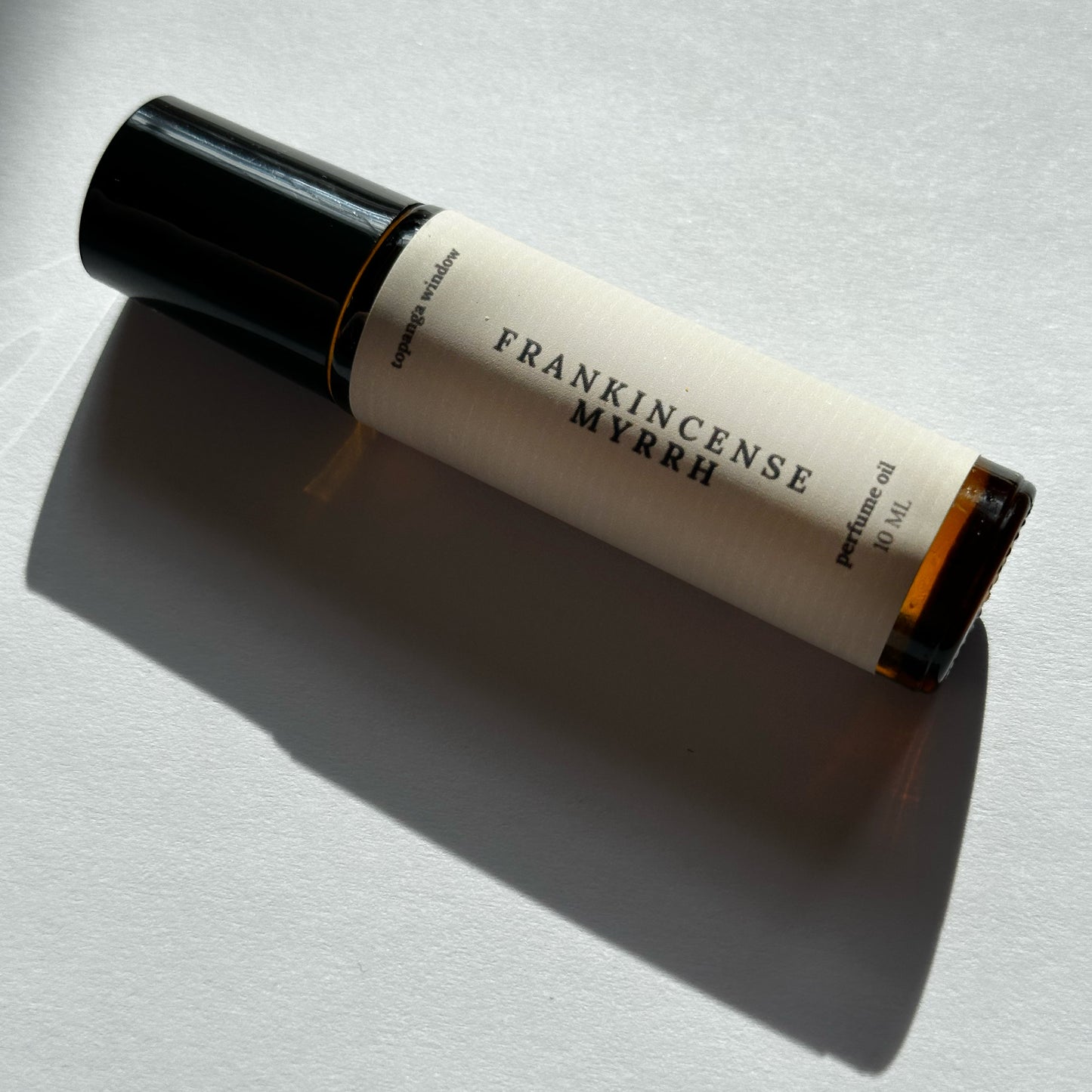 Roll-on bottle of Frankincense Myrrh perfume on a light background
