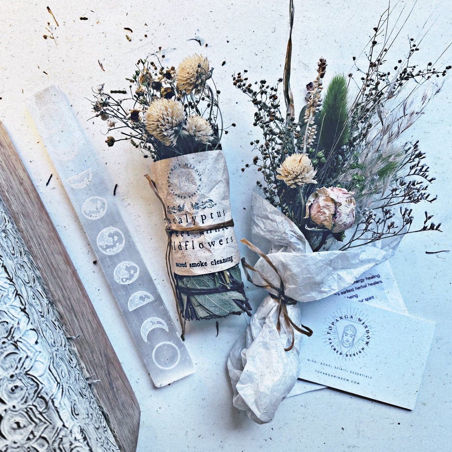 Decorative items including a book, candles, and dried flowers on a textured surface.