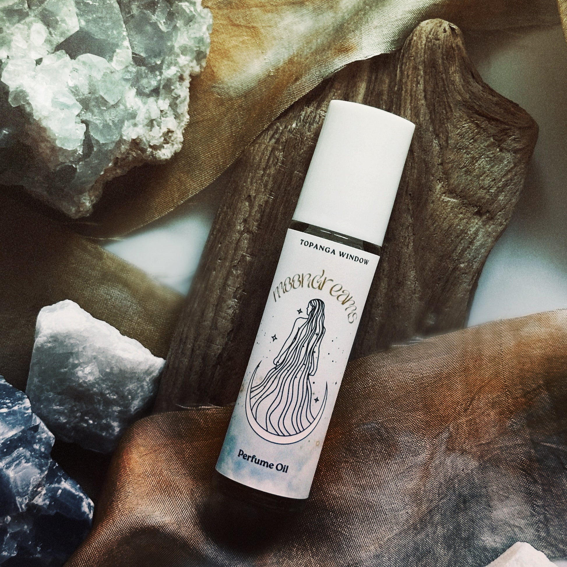 Perfume oil bottle labeled 'Moondreams' on a natural stone surface with crystals.