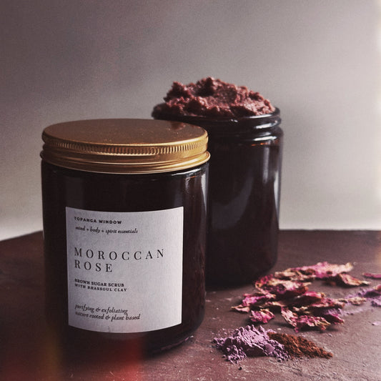 Jar of Moroccan Rose body scrub with a gold lid on a dark surface.