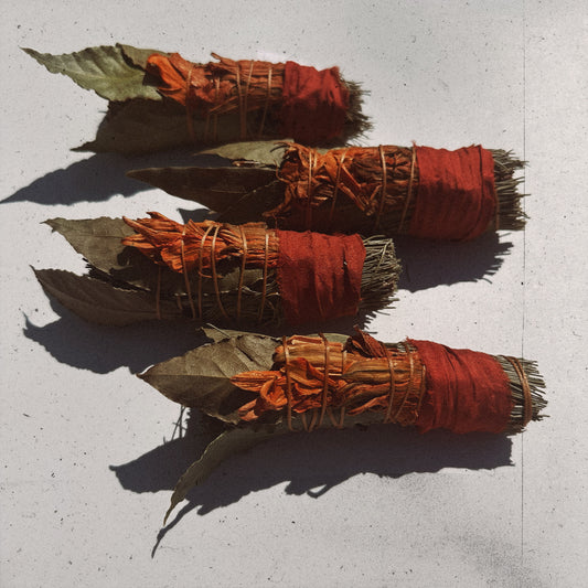 Three bundles of incense sticks with red fabric and leaves on a light gray background