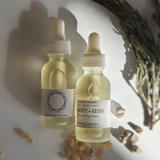 Two bottles of 'Root + Resin' essence with labels on a textured surface.