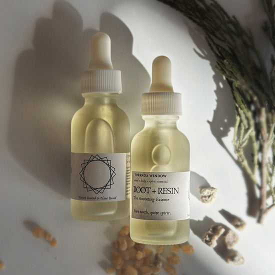 Two bottles of 'Root + Resin' essence with labels on a textured surface.