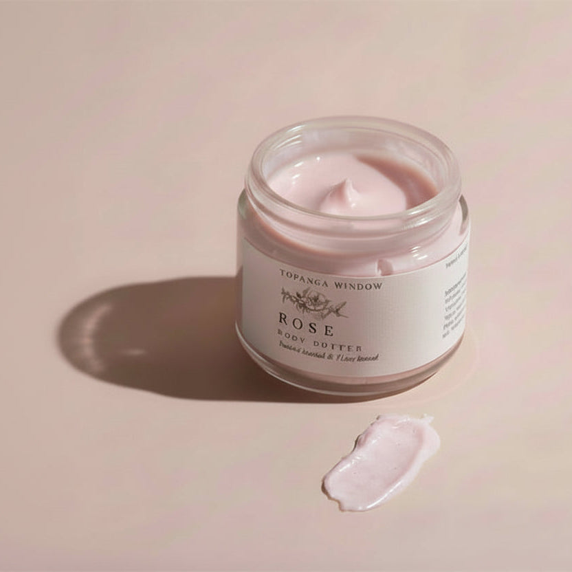 Jar of rose body butter on a light surface with soft shadows
