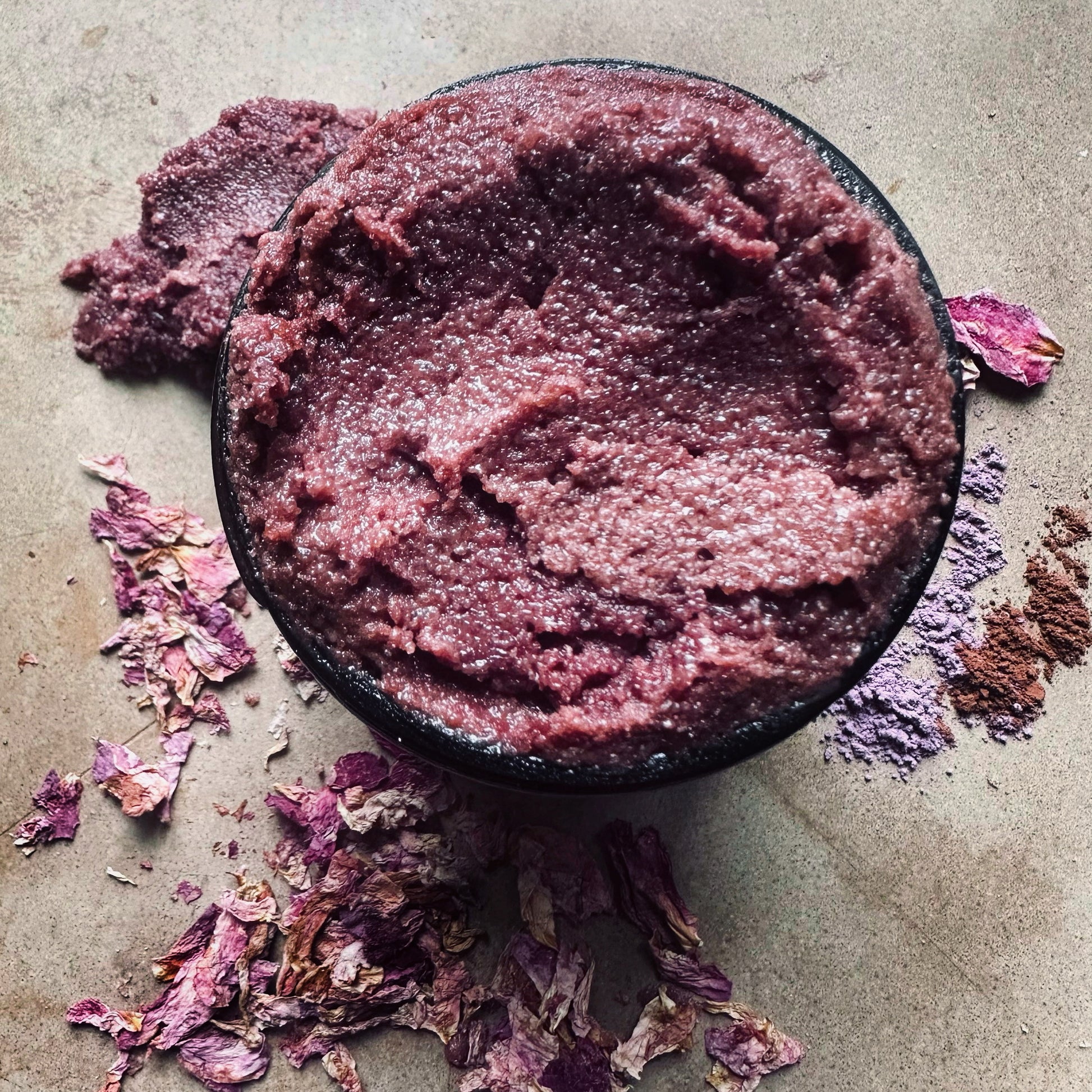 Purple scrub in a bowl with dried flowers on a textured surface