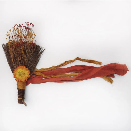 Decorative broom with red ribbons and a yellow flower on a white background