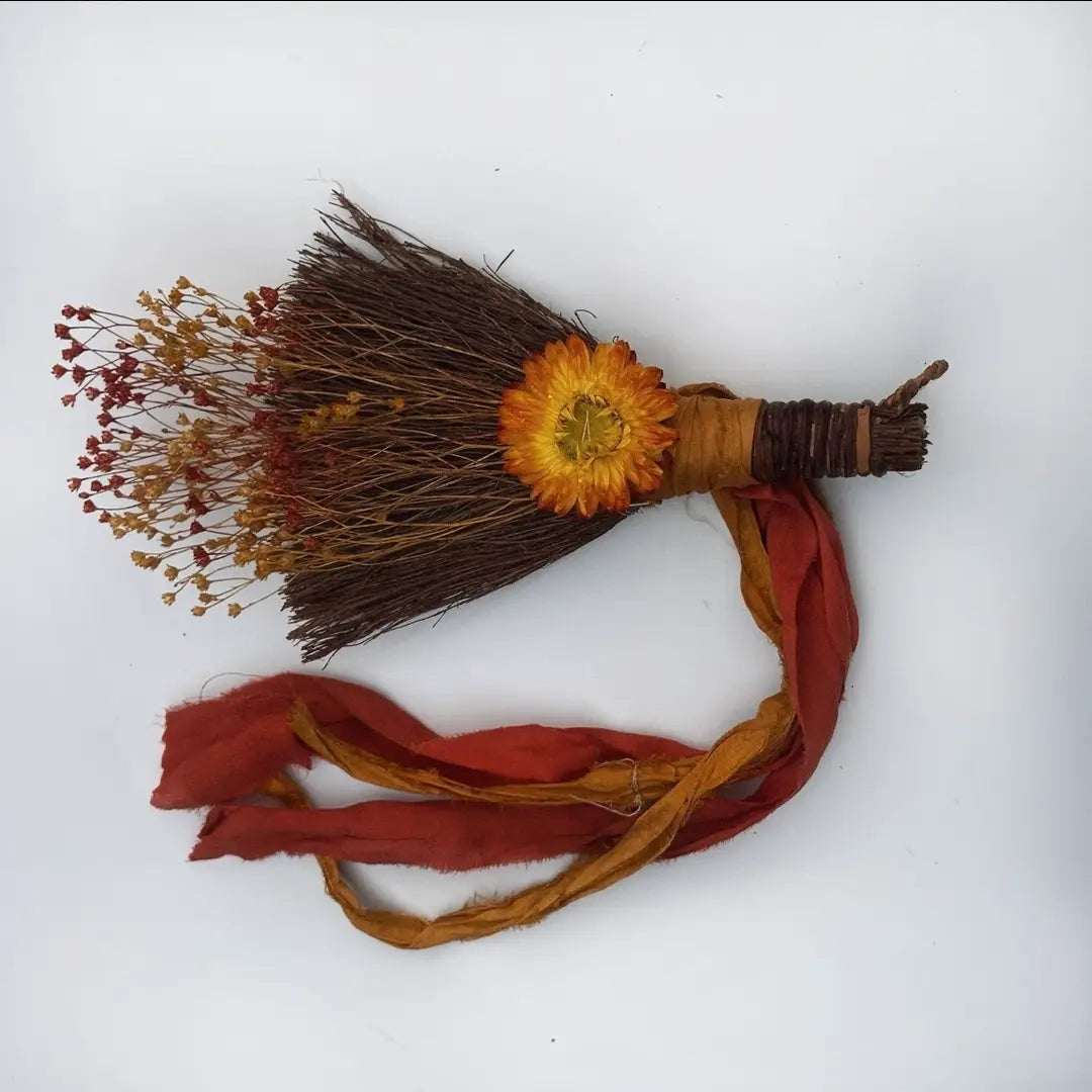 Decorative broom with orange flower and red fabric on a white background