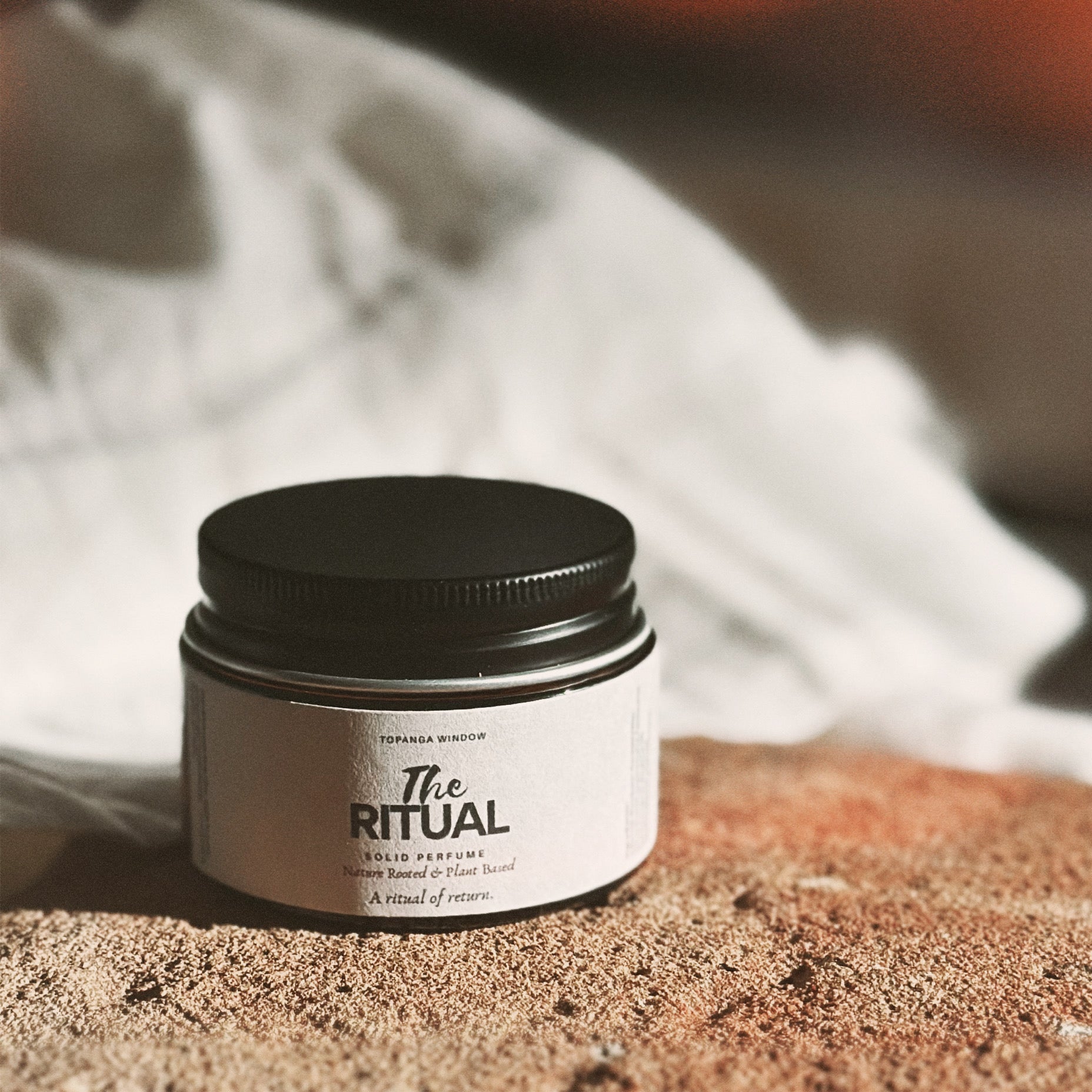Jar of 'The Ritual' solid perfume on a textured surface with a blurred background