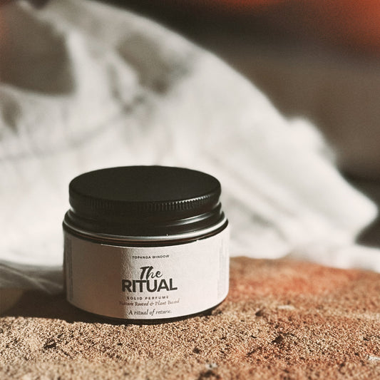 Jar of 'The Ritual' solid perfume on a textured surface with a blurred background