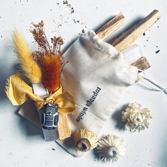 A set of Palo Santo sticks, white selenite crystals, and a Bolivian good luck amulet, all arranged on a surface with a yellow silk ribbon and a storage drawstring bag.